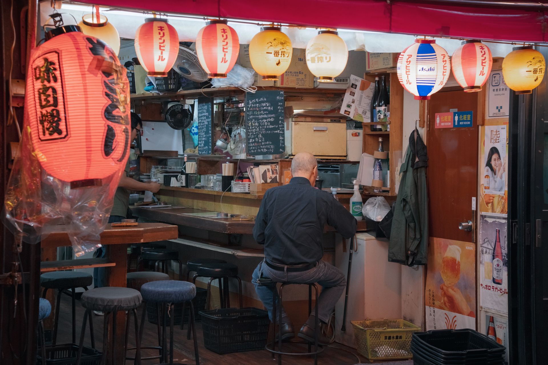 提灯が掛かった小さな居酒屋の店先でカウンターに座る客と店主