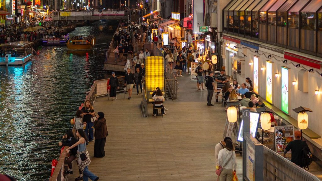 夜の道頓堀で川沿いに看板の明かりが並び人々が歩く通り
