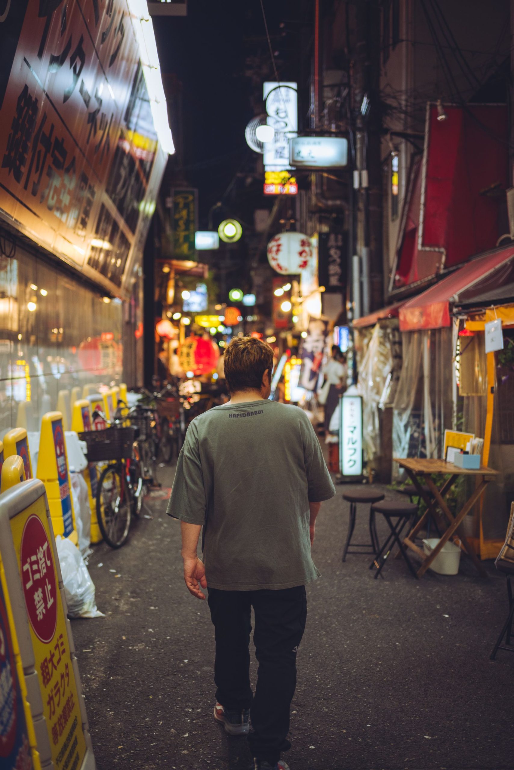 赤い光に照らされた夜の路地を一人で歩く人物の後ろ姿